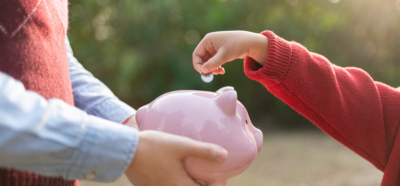 Un enfant met des pièces de monnaie dans la tirelire rose