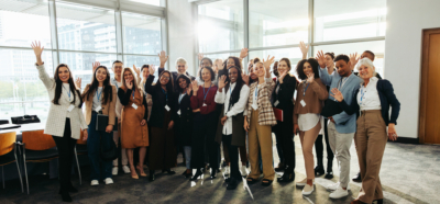 Groupe diversifié au séminaire saluant joyeusement à l’intérieur d’une salle de conférence moderne avec de grandes fenêtres et une lumière naturelle éclatante